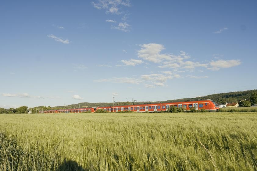 S-Bahn fährt durchs Remstal vor sommerlich wolkenbedecktem Himmel, im Vordergrund ein Getreidefeld